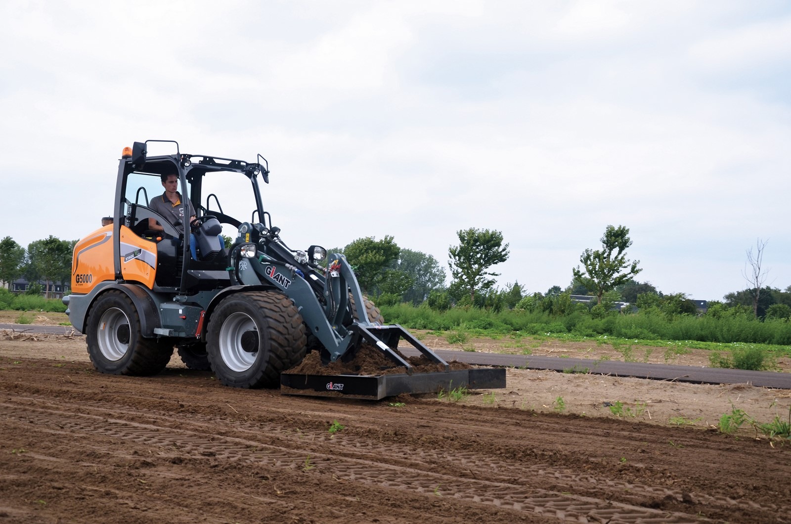 Ouvrier qui conduit la CHARGEUSE GIANT G5000 X-TRA avec son accessoire pour travailler la terre dans un champ